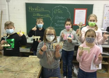 Kinder zeigen in einem Klassenraum Werkstücke aus Holz