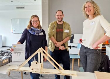 Drei Teilnehmende Fortbildung „KiTec –  Kinder entdecken Technik“ und ihr Bauwerk: eine Brücke aus Holz